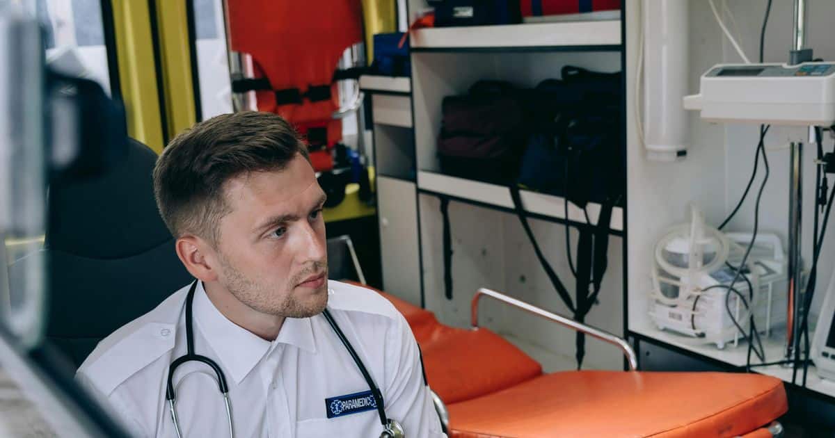 Paramedic with a stethoscope seated inside an ambulance beside a stretcher and mounted medical equipment